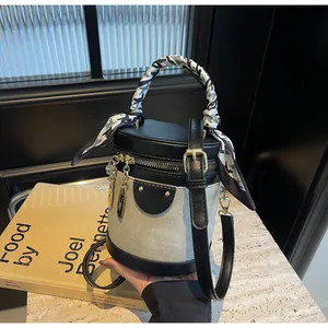 Detail of canvas bucket bag with black leather trim, decorative scarf, and gold hardware