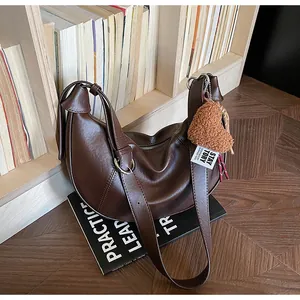 Détail du sac demi-lune en cuir marron foncé avec charm en peluche en forme de cœur