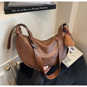 Détail d'un sac demi-lune marron foncé avec un ours en peluche et boucles en métal