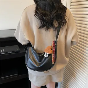 Sac à bandoulière noir en forme de croissant avec pendentif cœur marron sur un pull beige