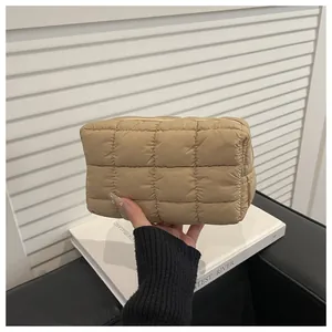 Gros plan sur une pochette matelassée beige tenue par un mannequin sur fond blanc