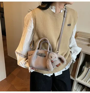 Detail of taupe textured leather bucket bag with silver clasp and plush bunny charm