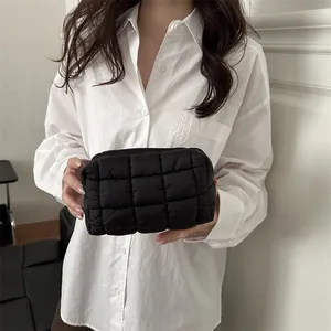 Pochette matelassée noire avec texture bouffante et fermeture éclair tenue par un mannequin