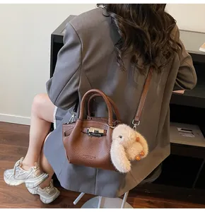 Detail view of brown lychee leather handbag with silver lock and plush rabbit charm