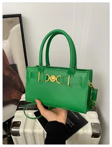 Detail of green crossbody bag with gold heart clasp held against travel suitcase