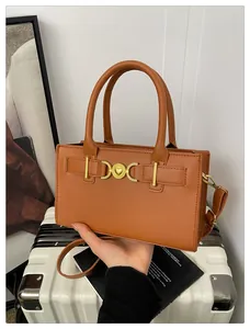 Detailed view of caramel brown handbag featuring a gold heart clasp on a white suitcase