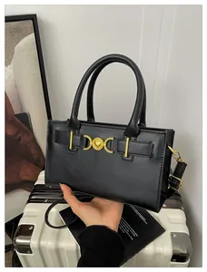 Detail of black leather crossbody bag featuring gold heart buckle and adjustable strap