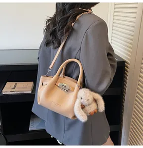 Detail view of beige lychee texture bucket bag with metal lock and plush rabbit charm