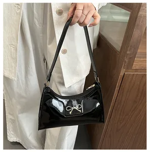 Detail of black patent leather handbag featuring a golden bow metal accessory and zip closure