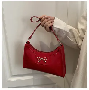 Détail du sac à main en cuir verni rouge avec boucle de nœud doré et fini brillant
