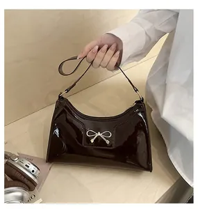 Vue détaillée du sac à main en cuir verni marron foncé avec boucle nœud dorée et zip