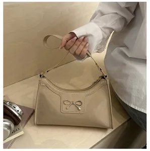 Detail of glossy beige patent leather bag with gold bow clasp and shoulder strap