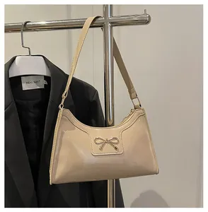 Détail du sac beige brillant avec un nœud en métal doré et une fermeture éclair