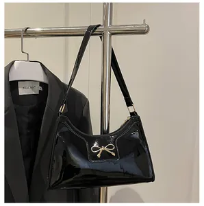Détail d'un sac à bandoulière en cuir verni noir brillant avec un nœud en métal chic