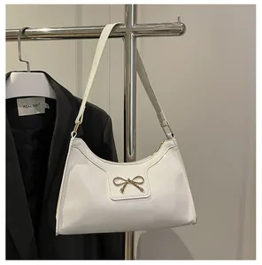 Vue détaillée d'un sac à main en cuir verni blanc crème avec un nœud en métal doré