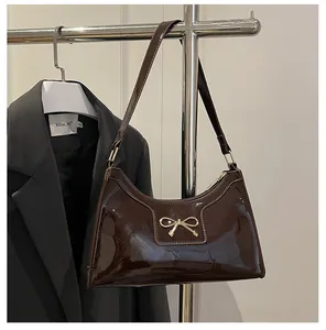 Détail d'un sac à bandoulière en cuir verni marron foncé brillant avec un nœud doré
