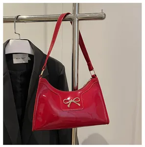 Gros plan du sac baguette en cuir verni rouge avec un nœud décoratif doré en métal