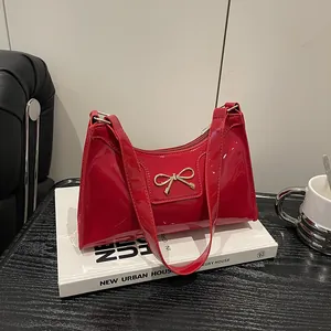 Sac à épaule en cuir verni rouge avec boucle nœud doré posé sur un livre élégant