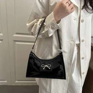 Sac sous l'aisselle en cuir verni noir avec nœud doré porté par un mannequin