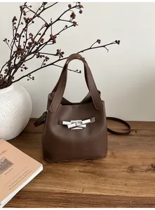 Détail du sac seau en cuir grainé marron foncé avec fermoir argenté sur une table en bois