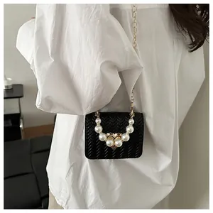 Close-up of black woven crossbody bag featuring pearl chain detail and gold heart hardware