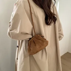Détail d'un sac nuage en daim marron avec plis et bandoulière porté sur un trench-coat