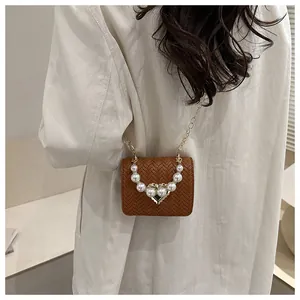 Detail of woven texture handbag featuring a pearl handle and heart-shaped gold clasp