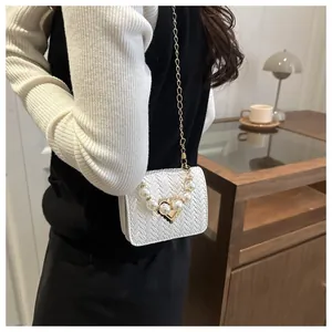 Detailed macro view of woven white faux leather and pearl heart emblem on the small handbag