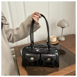 Detail view of black glossy leather handbag with gold metal buckles on a wooden table