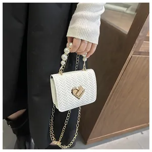 Detail of pearl handle and heart-shaped golden clasp on white woven crossbody bag