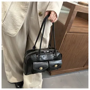 Detail of black glossy PU leather handbag with dual front pockets and gold metal buckles