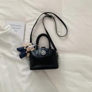 Dettaglio borsa nera a conchiglia con chiusura a scatto e ciondolo orsetto di peluche