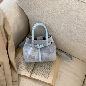 Detail of light blue leather handle and newspaper print canvas on a chic bucket bag