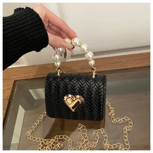 Detail of black woven leather handbag featuring gold heart lock and pearl handle accessory