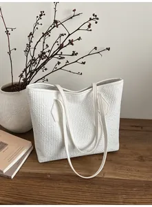 Détail d'un cabas blanc matelassé avec motifs géométriques posé sur une table en bois
