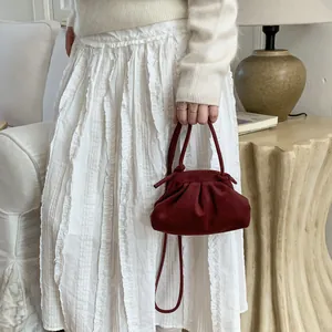Détail du sac à main plissé bordeaux en daim porté avec une tenue élégante en maille