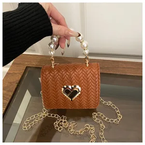Close-up of brown woven mini bag with heart lock, pearl handle, and gold chain strap