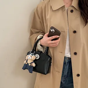 Elegante borsa a mano nera con ciondolo a forma di orsetto mostrata in una scena di strada