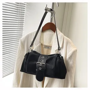 Détail d'un sac bandoulière noir plissé avec grande boucle métallique sur un blazer blanc