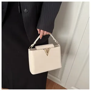 Dettaglio di borsa in pelle crema con vistosa fibbia in metallo dorato a forma di V