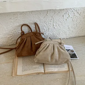 Détail de mini sacs nuages plissés en daim marron et beige posés sur un livre