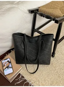 Détail d'un grand sac cabas noir avec texture en relief lézard posé contre une chaise