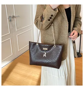 Detail of dark brown woven tote bag featuring a golden deer charm and chain strap