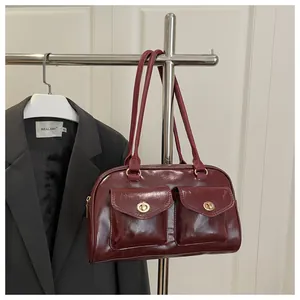 Detail of burgundy glossy handbag with dual front pockets and gold turn-lock closures