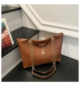 Detail of brown woven texture tote bag featuring a gold chain strap and deer charm