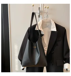 Détail du cabas en cuir noir mat avec lettrage doré et bandoulière longue sur veste de costume