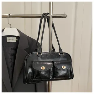 Detail of glossy black shoulder bag with gold metal buckles on double front pockets