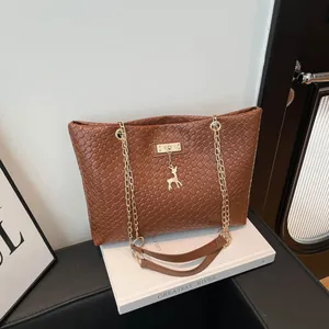 Elegant brown woven bucket bag with gold chain strap and deer pendant on white book