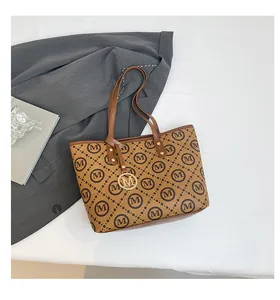 Détail d'un sac cabas marron avec imprimé M et breloque logo dorée sur un blazer élégant