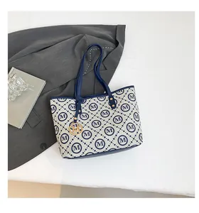 Détail du sac cabas à motif M bleu avec pendentif doré et poignées en cuir élégantes